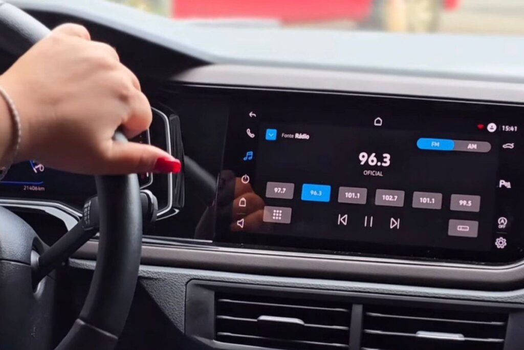 Painel multimídia de um carro sintonizado na frequência 96,3 FM, destacando a audiência do rádio durante deslocamentos e horários de pico no trânsito.